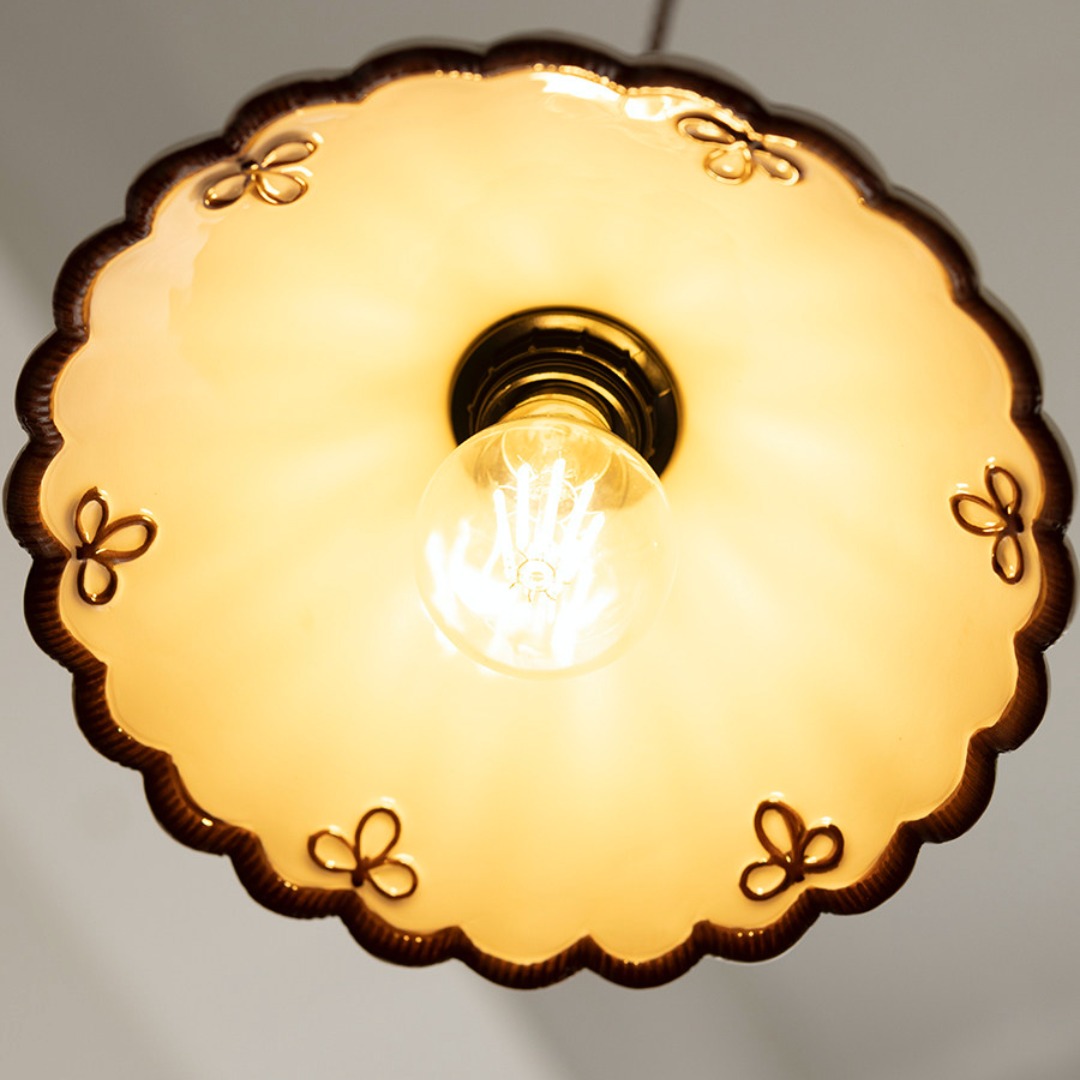 Detalle iluminado de la parte inferior de una pantalla colgante de cerámica con forma de concha.