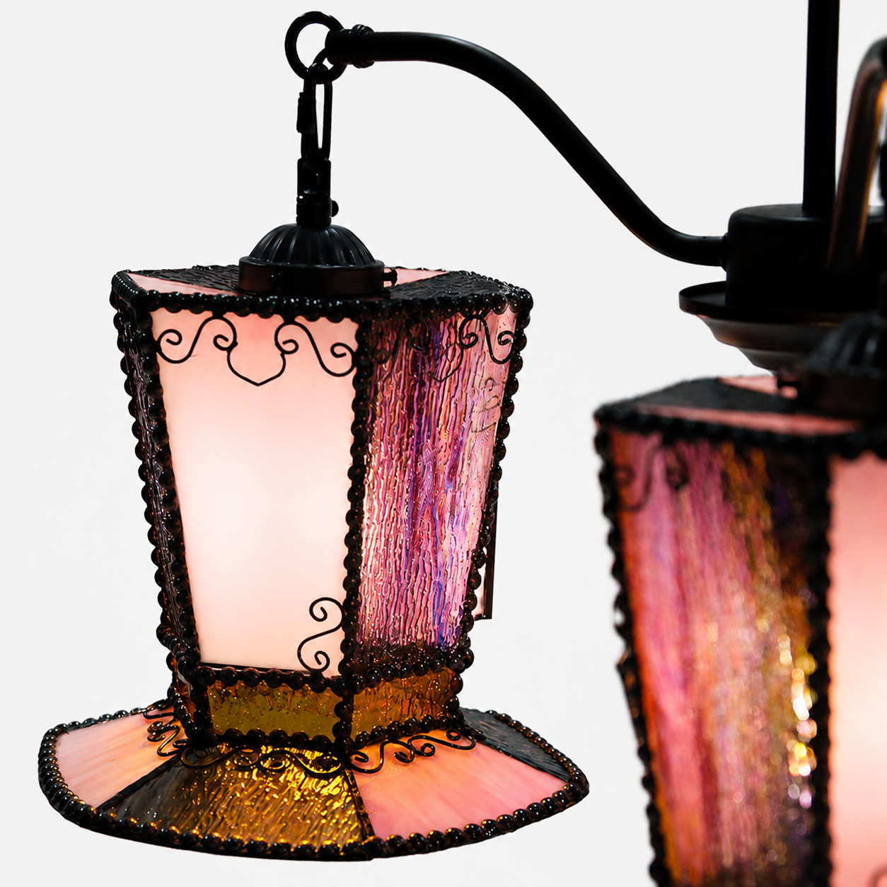 Gros plan sur l'abat-jour en verre du lustre, la bordure en métal noir et les détails en volutes