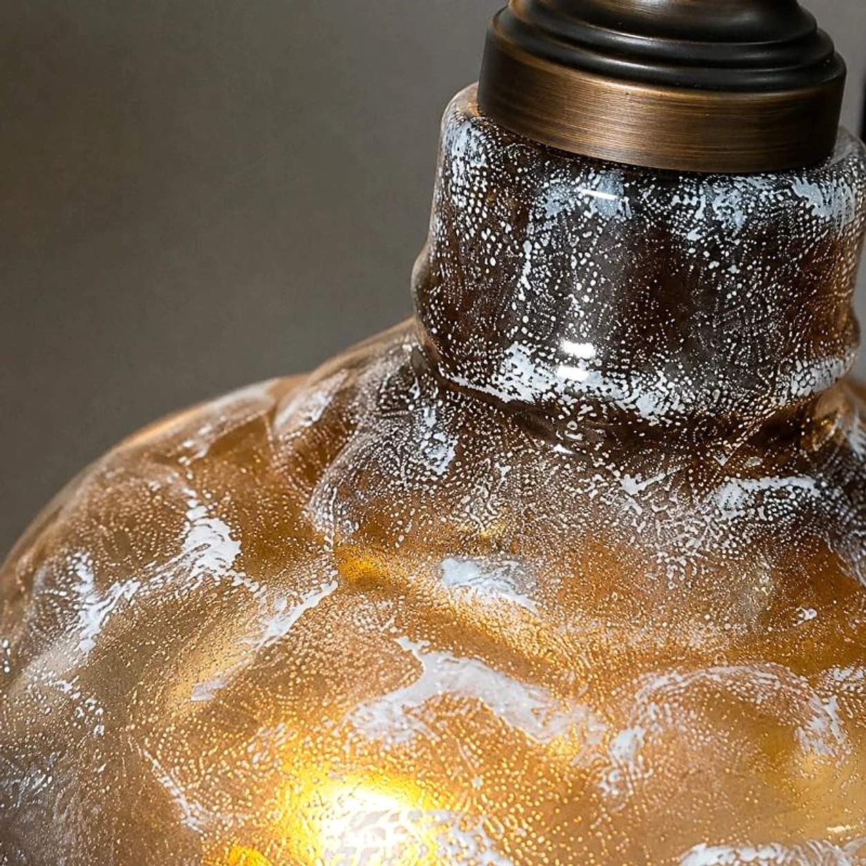 Gros plan sur un abat-jour en verre texturé gris fumé aux reflets ambrés chauds.