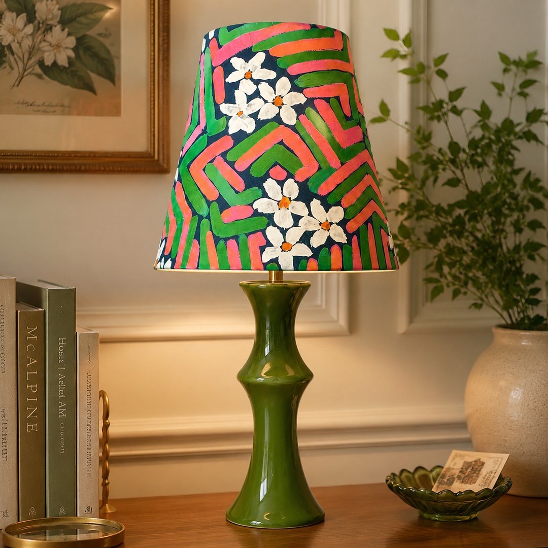 Lámpara de mesa rosa y verde brillando junto a un arte de pared enmarcado