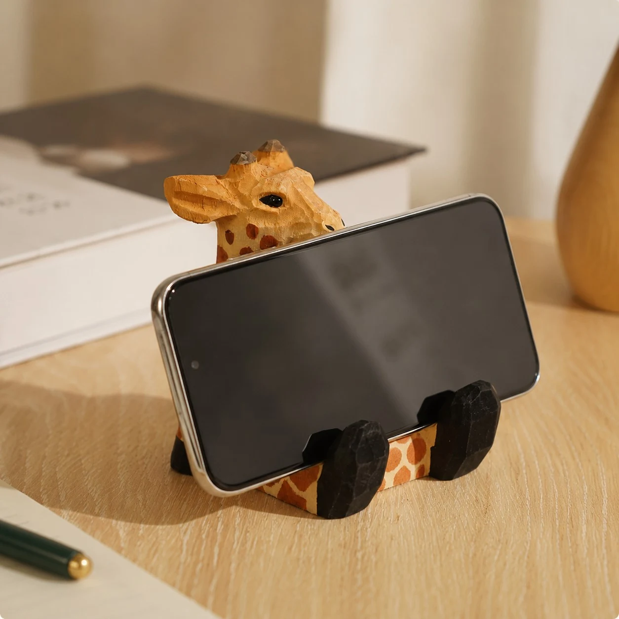 Supporto per cellulare in legno a forma di giraffa che regge un telefono su una scrivania.