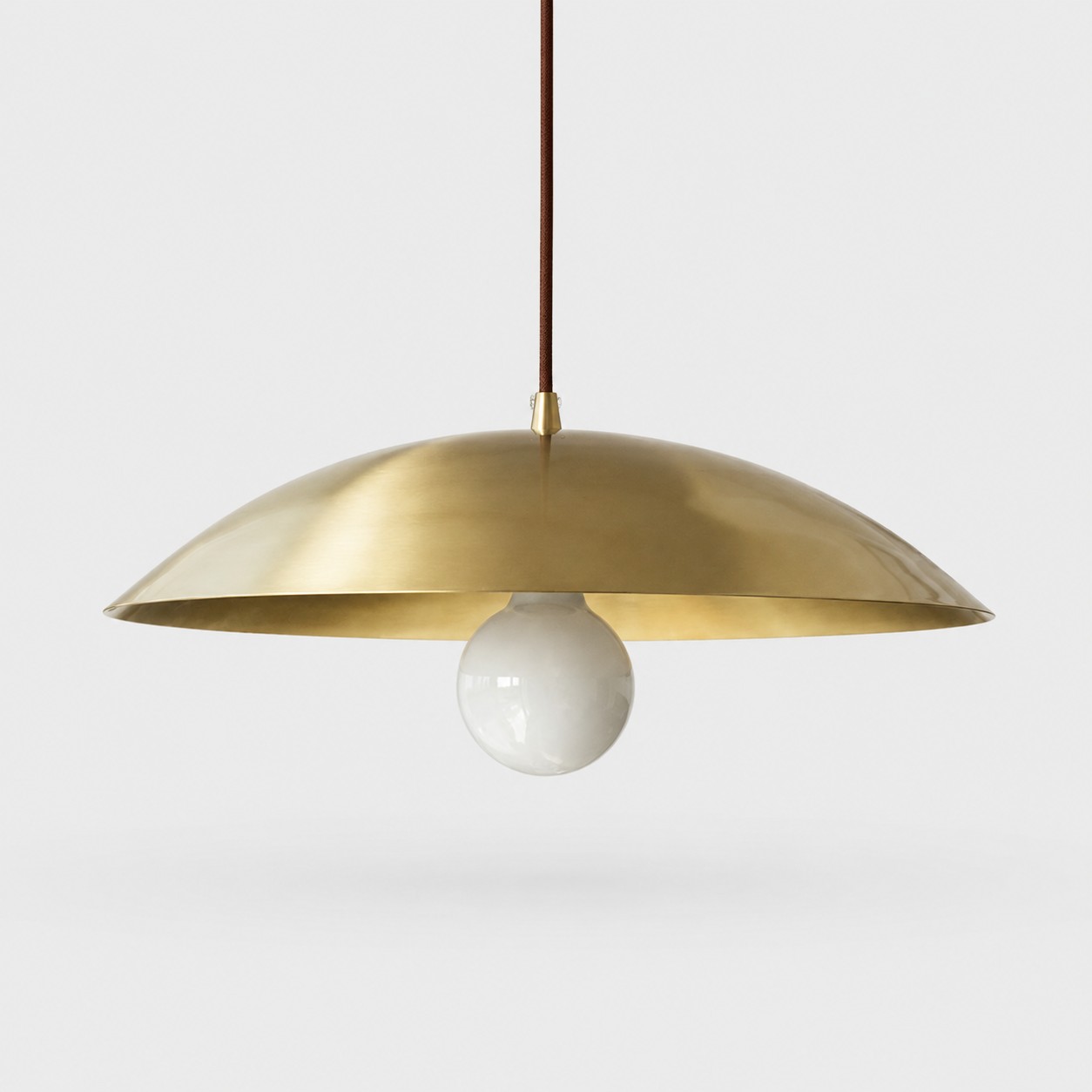 Lampada a sospensione a cupola in ottone spazzolato su sfondo grigio neutro.