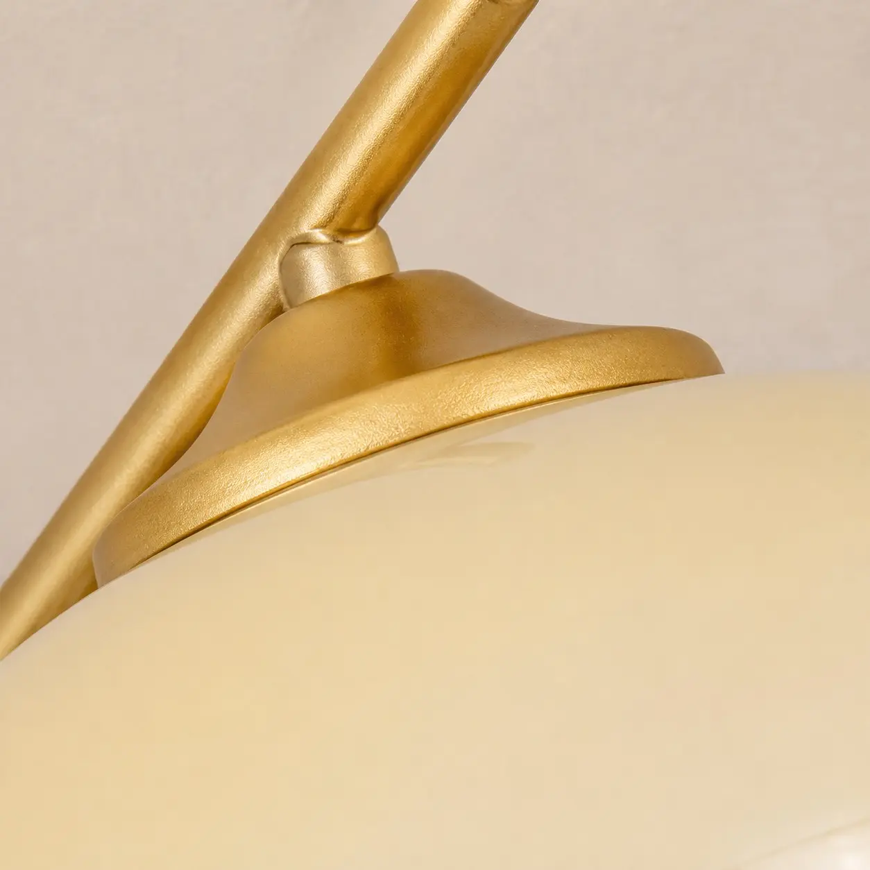 Detail zlatého ramene lampy a bílého skleněného stínidla