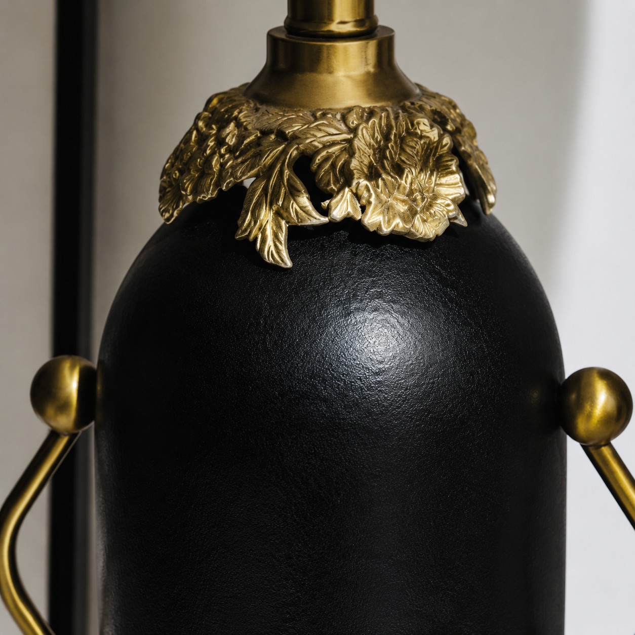 Primo piano del corpo della lampada in nero opaco e dei dettagli floreali color ottone.