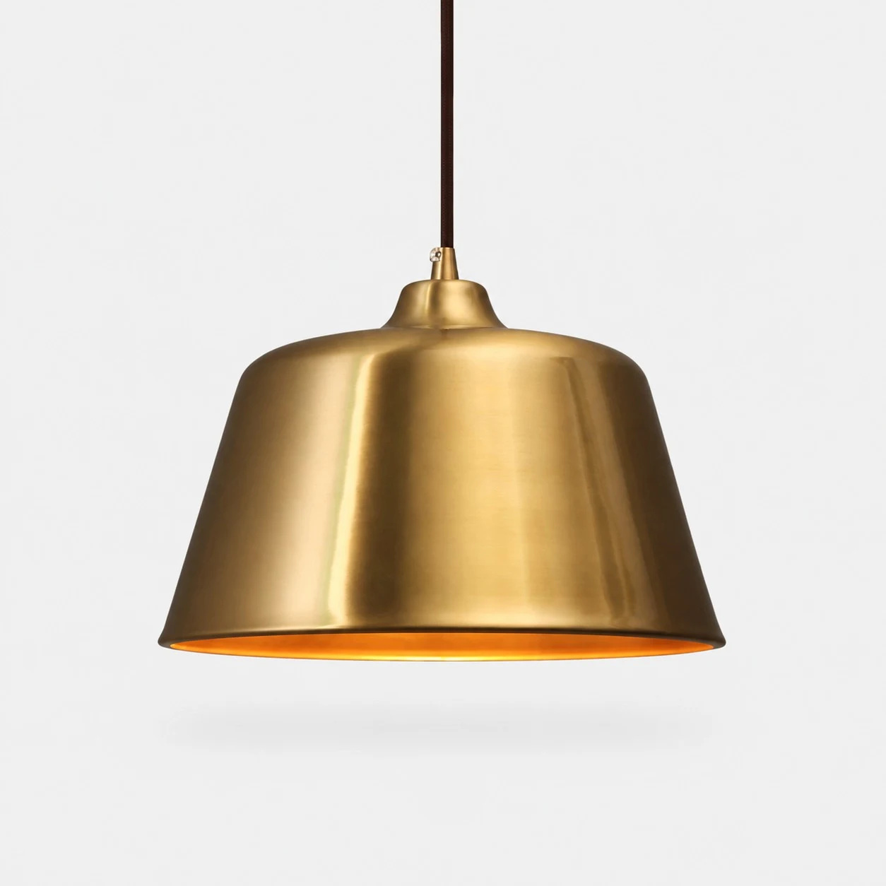 Luminária pendente em forma de sino, em latão brilhante, sobre um fundo neutro.