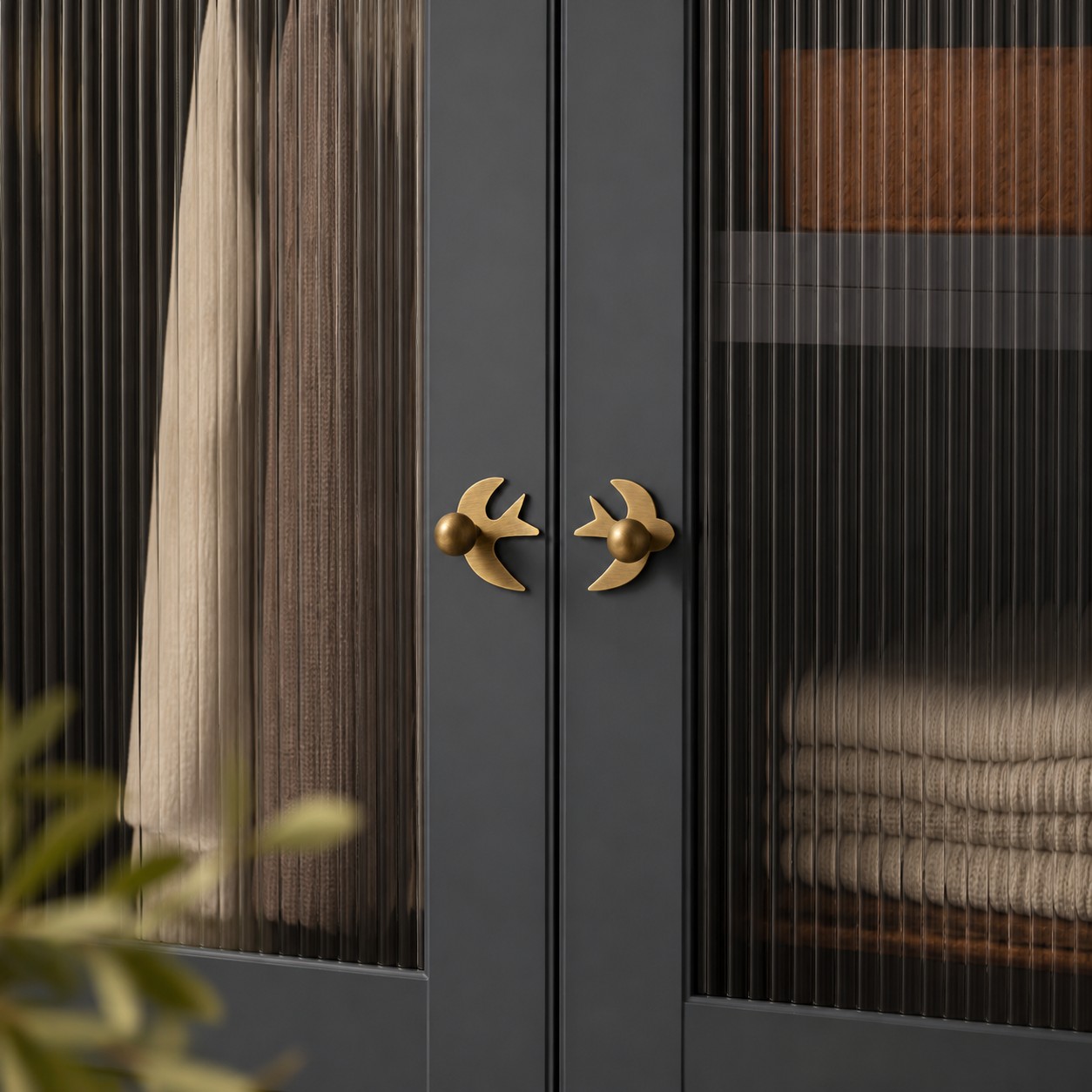 Antique brass swallow handles on a dark glass-front cabinet