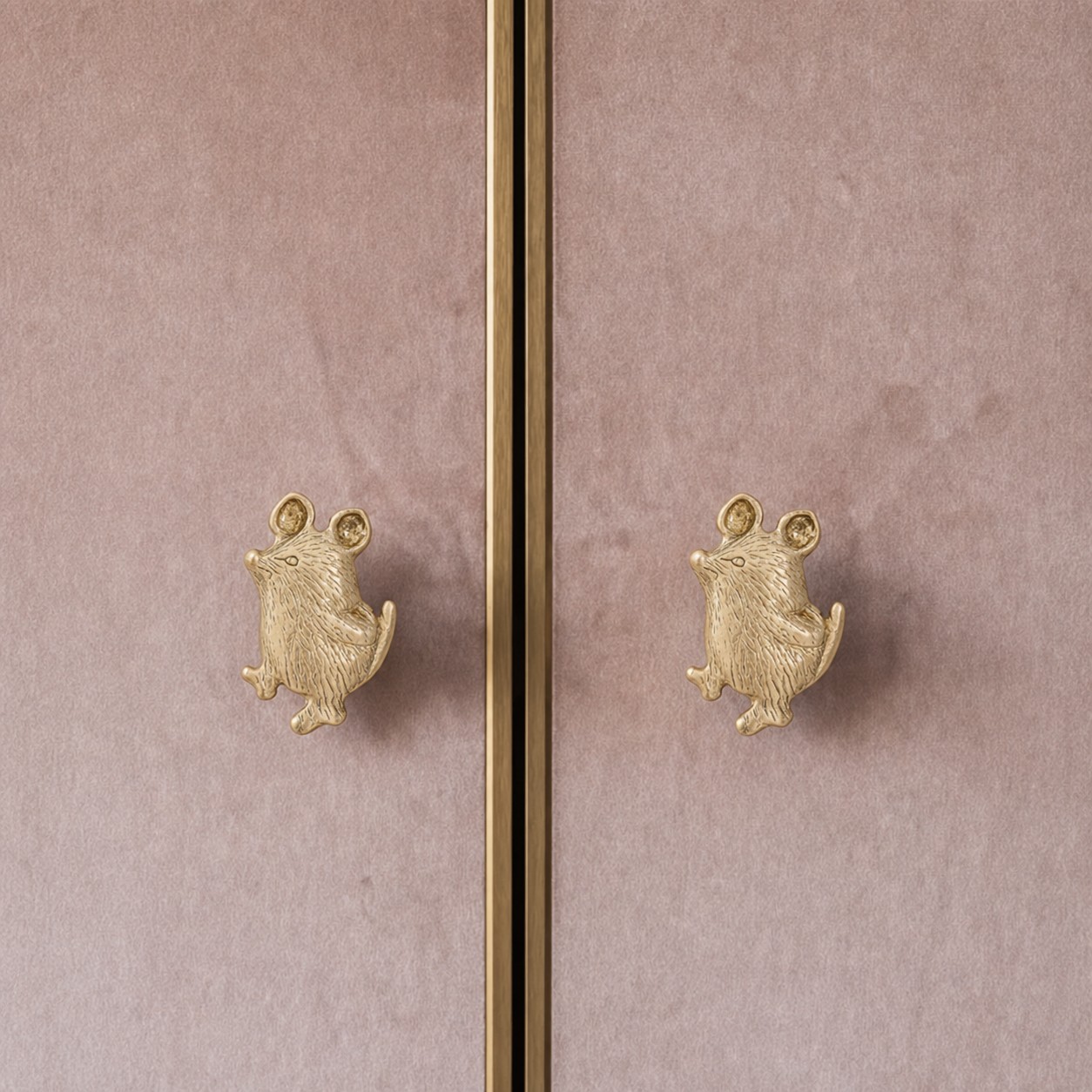 Pair of brass mouse cabinet knobs on a pink cabinet