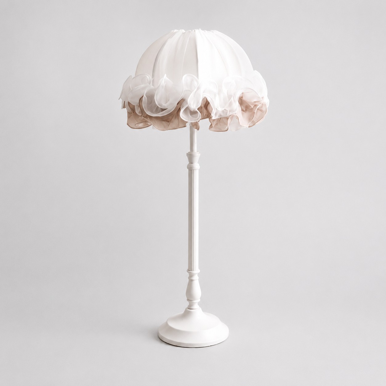Vue de face d'une lampe de table en tissu blanc à volants avec un pied en métal sculpté